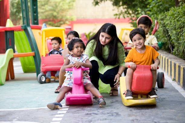Female teacher with preschool children riding toy rocking horse